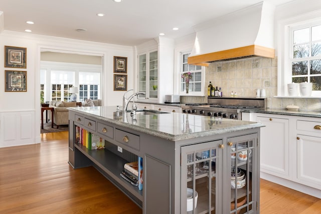 kitchen with premium range hood, sink, a center island with sink, and white cabinets