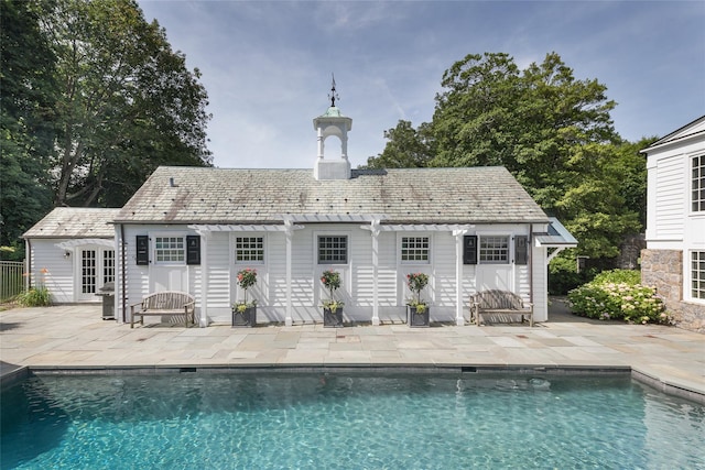 rear view of property with a patio, a high end roof, an outdoor pool, an outdoor structure, and a storage structure