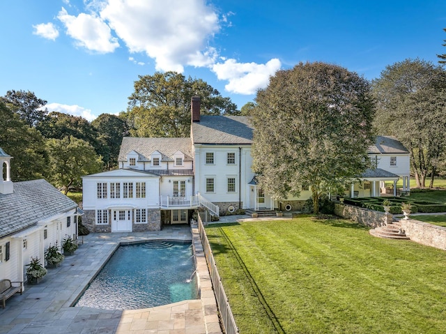 rear view of property featuring pool water feature, a balcony, a lawn, a fenced in pool, and a patio