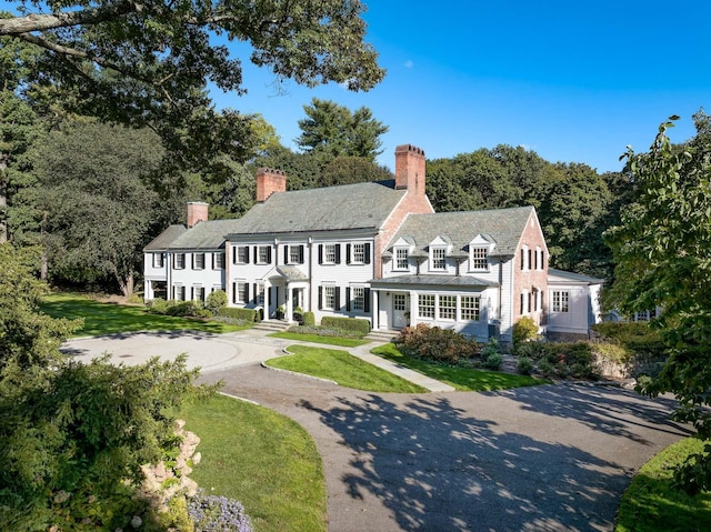 view of front of house with aphalt driveway, a chimney, and a front yard