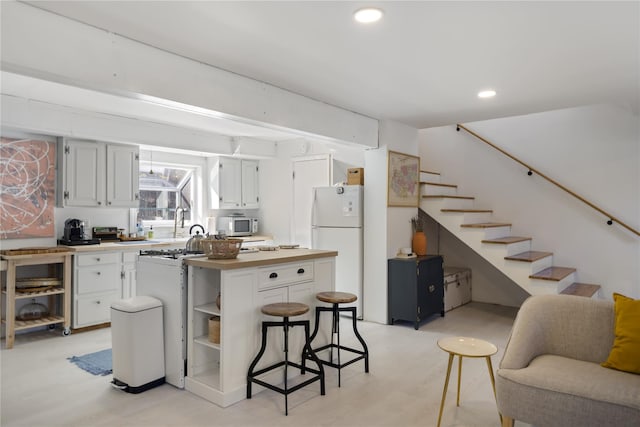 kitchen with a breakfast bar, white cabinetry, white appliances, and light hardwood / wood-style flooring