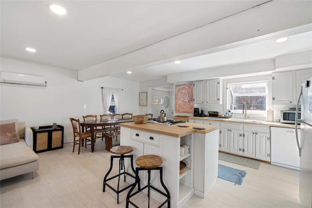 kitchen featuring butcher block counters, white cabinetry, sink, stainless steel appliances, and a wall mounted AC