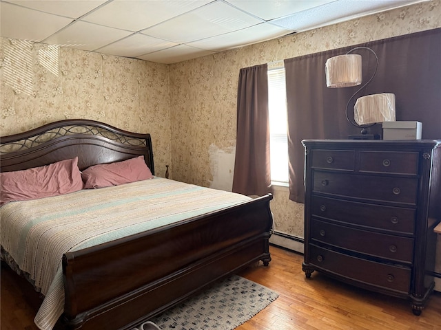 bedroom featuring baseboard heating, a paneled ceiling, and light hardwood / wood-style flooring