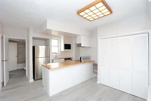 kitchen featuring light wood-type flooring, a sink, wood counters, freestanding refrigerator, and a peninsula