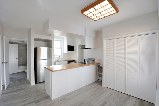 kitchen with a peninsula, light wood-style flooring, freestanding refrigerator, a sink, and butcher block counters