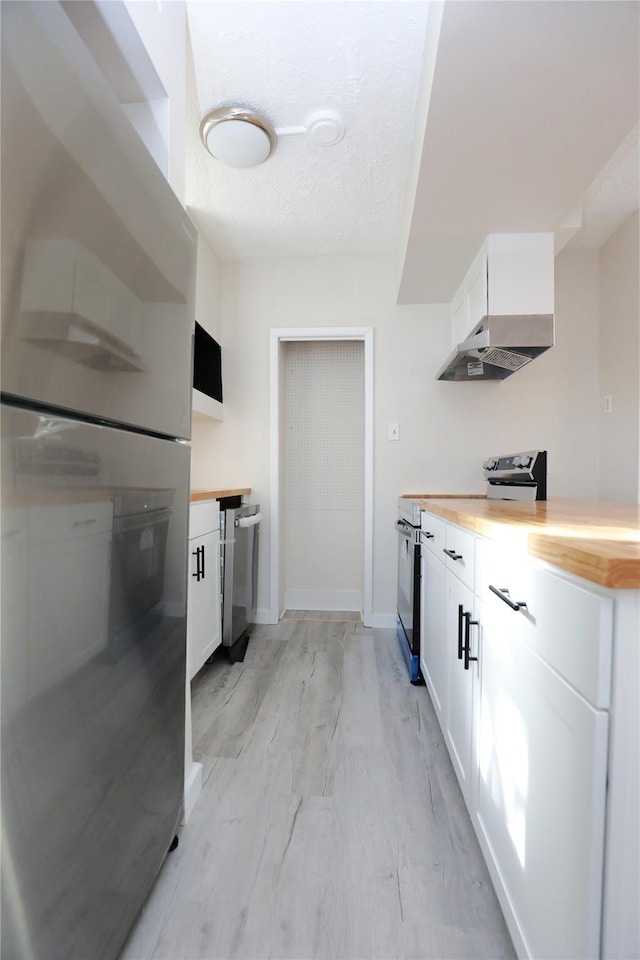 kitchen featuring under cabinet range hood, white cabinets, appliances with stainless steel finishes, and butcher block countertops