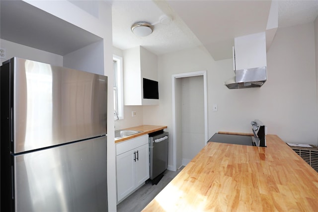 kitchen with wooden counters, white cabinetry, range hood, stainless steel appliances, and a sink