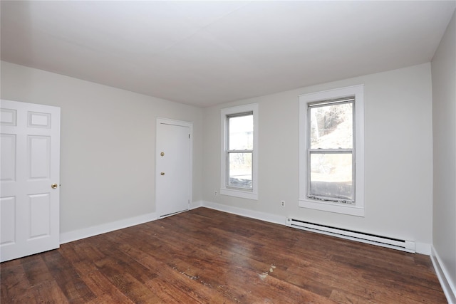 empty room with a baseboard heating unit, baseboards, and wood finished floors