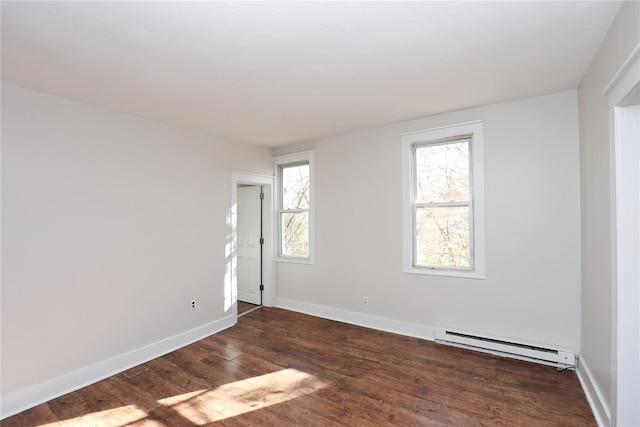 empty room featuring a baseboard heating unit, wood finished floors, and baseboards