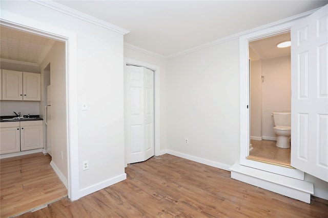 unfurnished bedroom with baseboards, a sink, light wood-style floors, crown molding, and connected bathroom