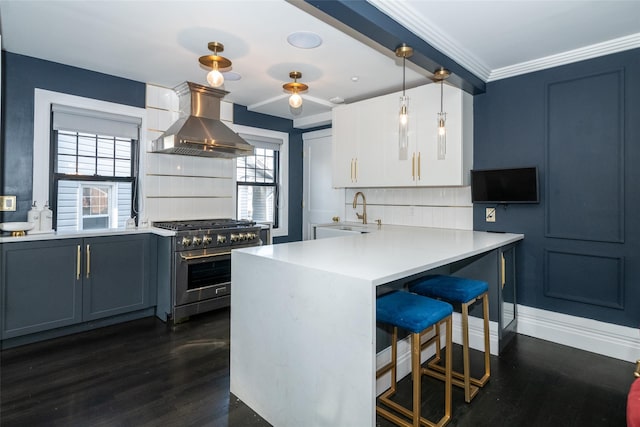 kitchen featuring pendant lighting, sink, wall chimney exhaust hood, stainless steel range, and white cabinetry