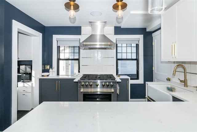 kitchen featuring a wealth of natural light, sink, wall chimney exhaust hood, high end stainless steel range oven, and white cabinets