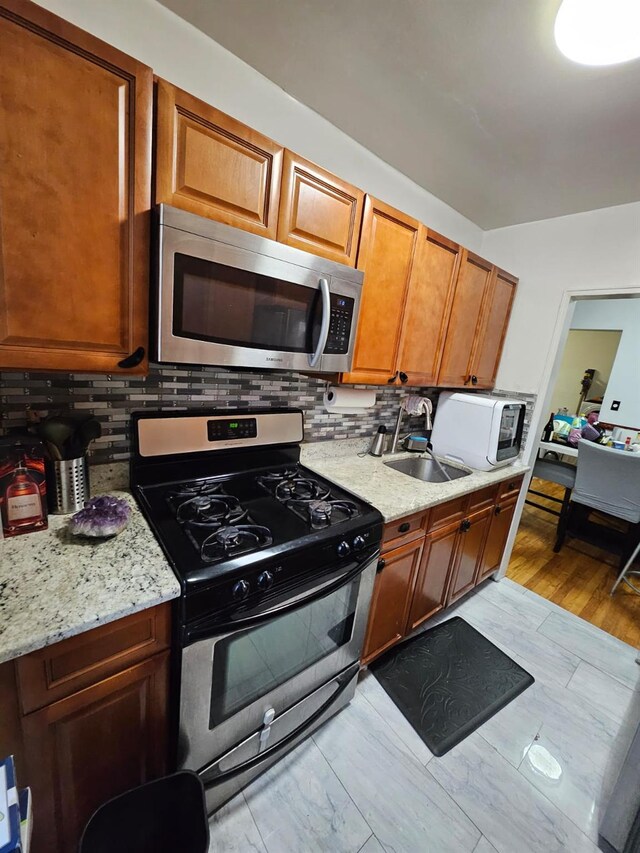 2750 Olinville Ave Unit 4H, Bronx, NY 10467 - kitchen featuring appliances with stainless steel finishes, tasteful backsplash, brown cabinetry, light wood finished floors, and light stone countertops