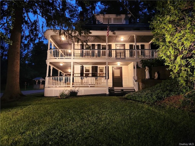 back house at twilight with a lawn, a balcony, and a porch