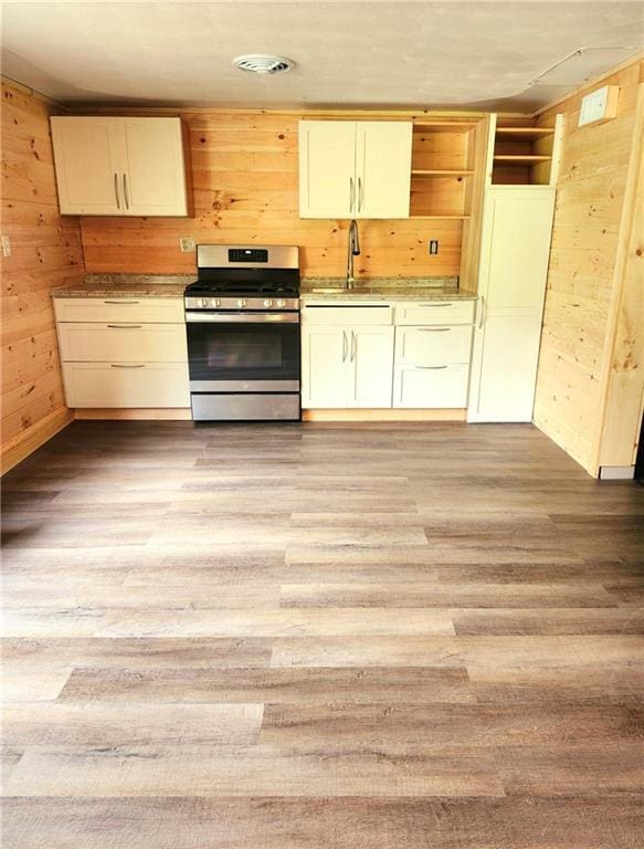 kitchen featuring wood walls, stainless steel gas stove, sink, and light wood-type flooring