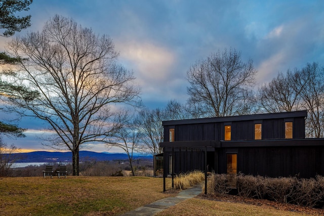 back house at dusk featuring a mountain view and a lawn