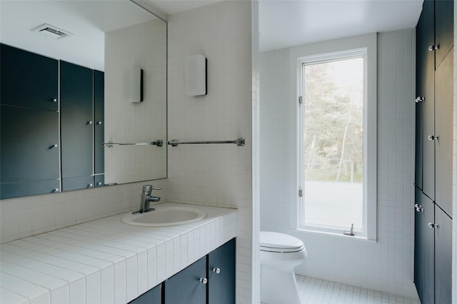 bathroom featuring vanity, toilet, tile patterned flooring, and tile walls