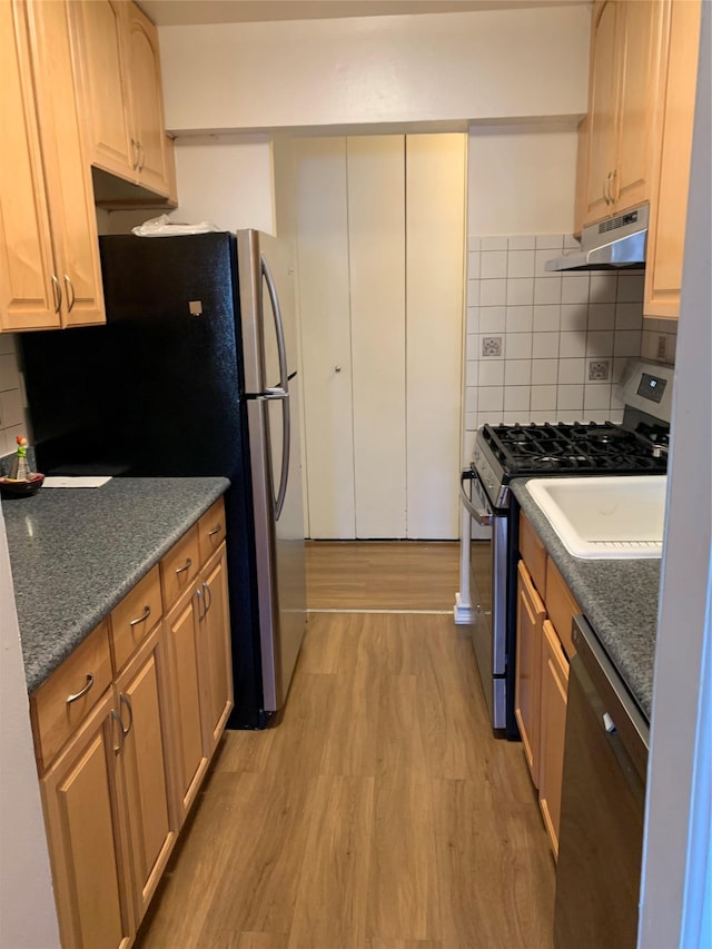 kitchen with decorative backsplash, light brown cabinets, stainless steel appliances, and light hardwood / wood-style flooring