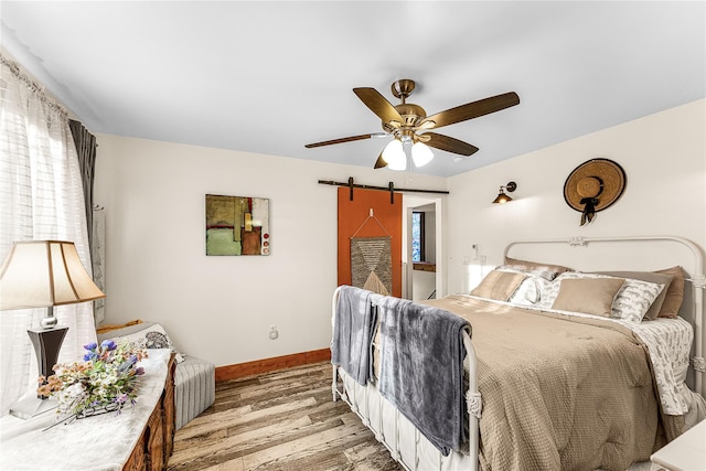 bedroom featuring hardwood / wood-style floors, a barn door, multiple windows, and ceiling fan