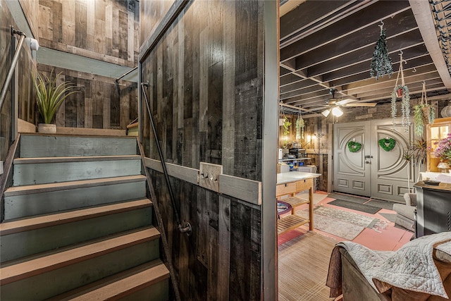 staircase featuring french doors, ceiling fan, and wood walls