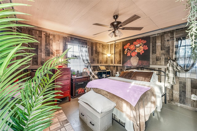 bedroom with ceiling fan, wood walls, and concrete flooring