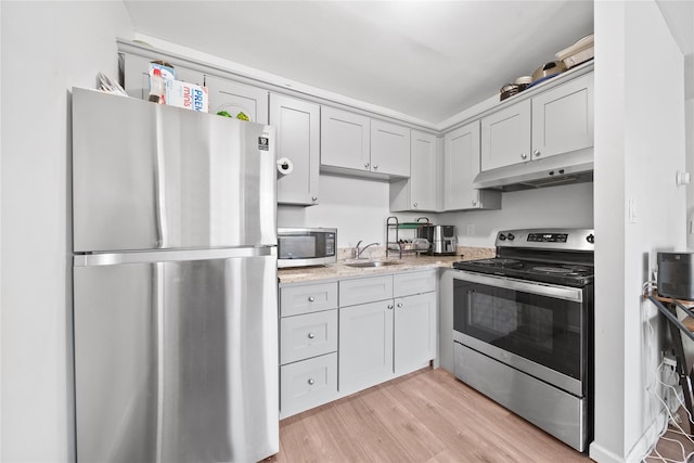 kitchen with light stone countertops, appliances with stainless steel finishes, light hardwood / wood-style flooring, and sink