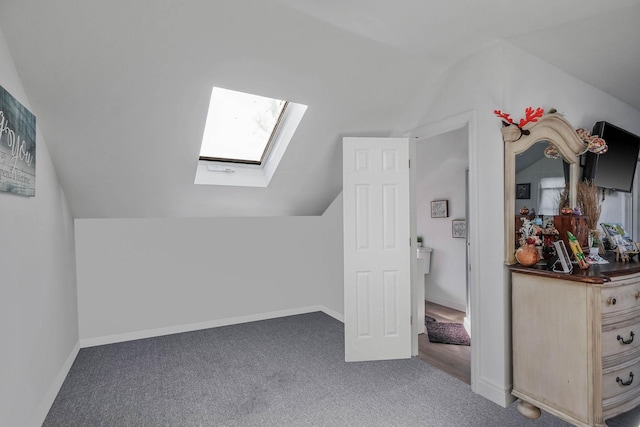 additional living space with dark colored carpet and vaulted ceiling with skylight