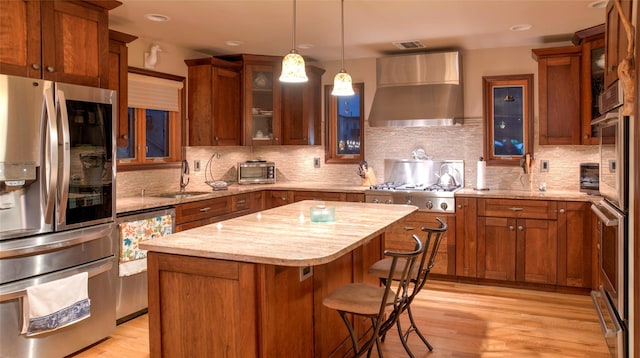 kitchen with sink, wall chimney exhaust hood, stainless steel appliances, a kitchen island, and light wood-type flooring