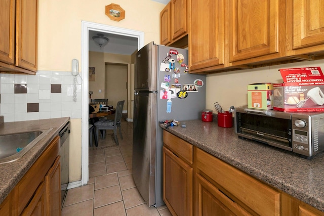 kitchen featuring sink, backsplash, dark stone countertops, light tile patterned floors, and appliances with stainless steel finishes