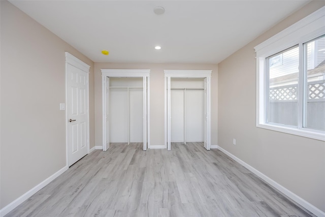 unfurnished bedroom featuring light hardwood / wood-style flooring and two closets