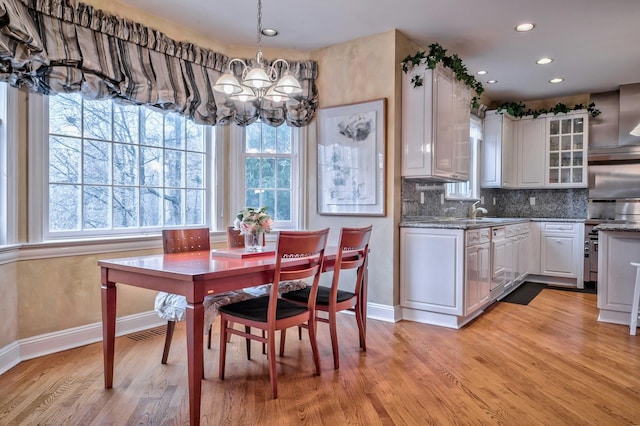 kitchen featuring pendant lighting, stainless steel stove, light wood-type flooring, stone countertops, and white cabinetry