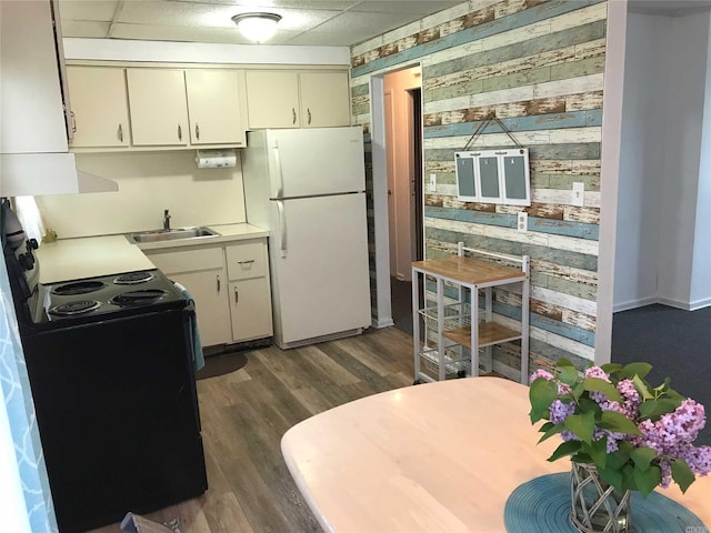 kitchen featuring black range with electric stovetop, sink, wooden walls, white fridge, and dark hardwood / wood-style flooring