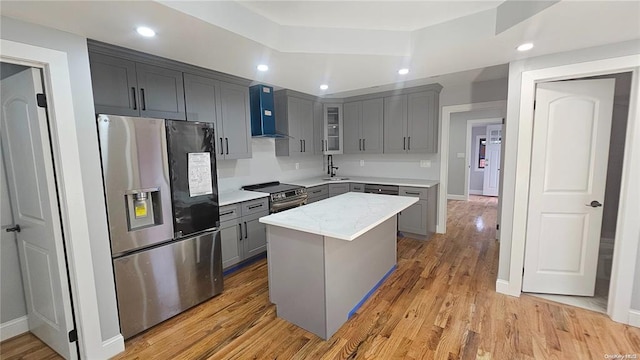 kitchen featuring a center island, wall chimney range hood, stainless steel appliances, and light hardwood / wood-style flooring