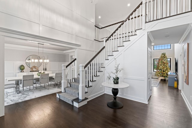 stairs with crown molding, wood-type flooring, an inviting chandelier, and a towering ceiling