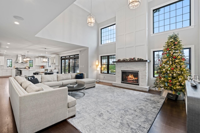 living room featuring a notable chandelier, a stone fireplace, dark wood-type flooring, and a high ceiling