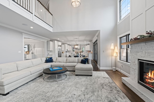 living room featuring dark hardwood / wood-style flooring, a stone fireplace, a wealth of natural light, and an inviting chandelier