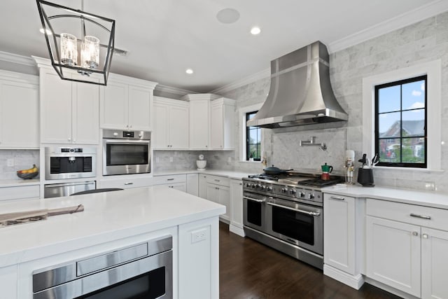 kitchen with white cabinetry, wall chimney range hood, crown molding, and appliances with stainless steel finishes