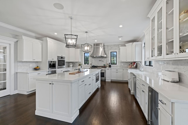 kitchen with a kitchen island, white cabinets, hanging light fixtures, stainless steel appliances, and wall chimney exhaust hood