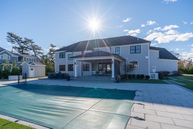 rear view of property with a storage unit, a covered pool, a patio, and central air condition unit