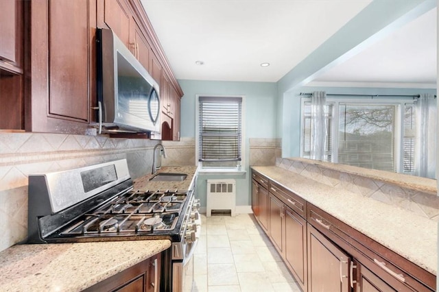 kitchen featuring light stone countertops, stove, decorative backsplash, radiator, and sink