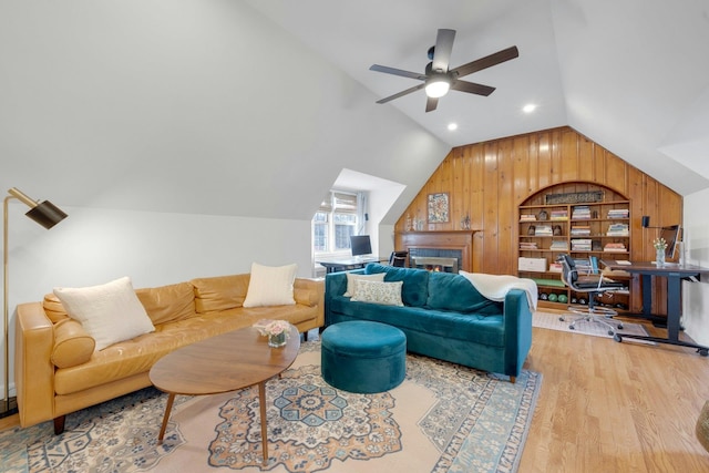 living room featuring ceiling fan, built in features, light hardwood / wood-style flooring, wood walls, and lofted ceiling