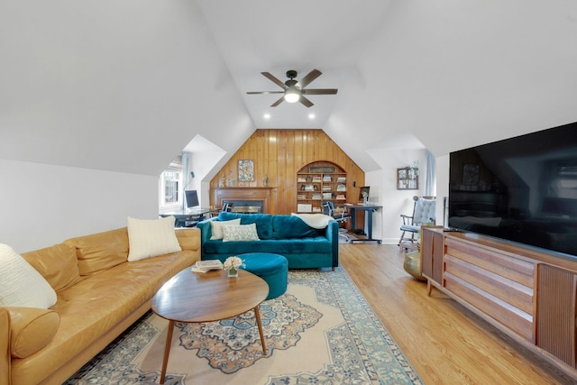 living room featuring ceiling fan, wood walls, vaulted ceiling, and light wood-type flooring