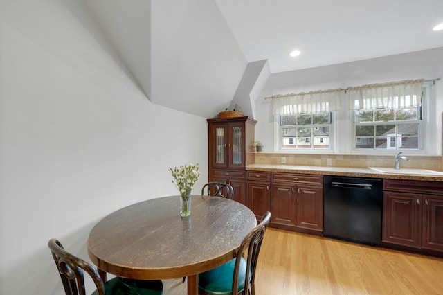 kitchen featuring tasteful backsplash, light stone counters, sink, black dishwasher, and light hardwood / wood-style floors