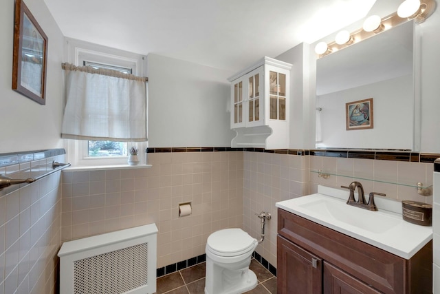 bathroom featuring radiator heating unit, tile patterned floors, toilet, vanity, and tile walls