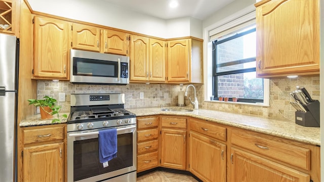 kitchen with decorative backsplash, light stone counters, sink, and appliances with stainless steel finishes