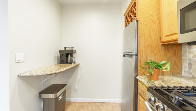 kitchen featuring light stone counters, backsplash, light brown cabinetry, light tile patterned flooring, and appliances with stainless steel finishes