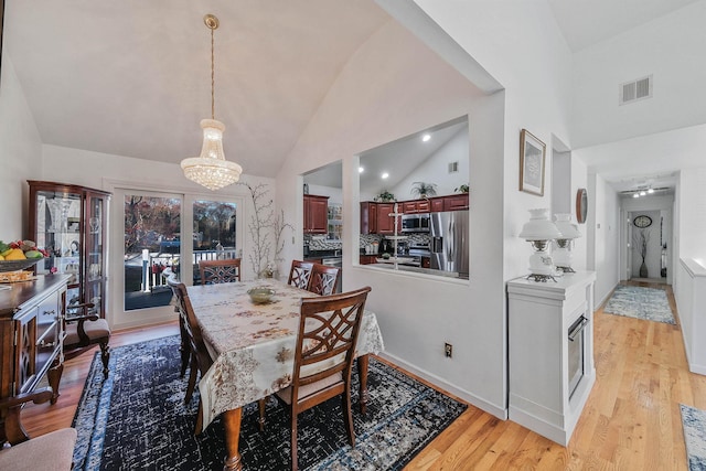 dining space with high vaulted ceiling, a chandelier, and light wood-type flooring