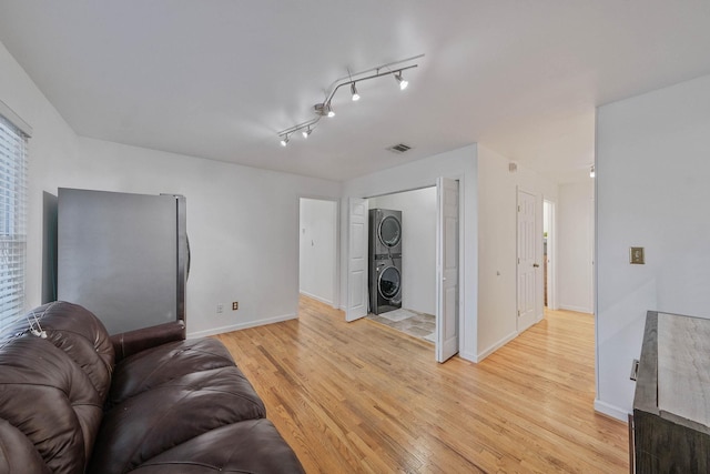 living room featuring track lighting, light hardwood / wood-style flooring, and stacked washer and clothes dryer