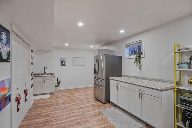 kitchen featuring light stone countertops, stainless steel refrigerator with ice dispenser, sink, light hardwood / wood-style flooring, and white cabinetry