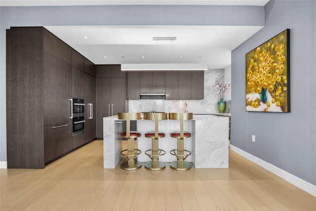 kitchen with tasteful backsplash, a breakfast bar, a center island, and light hardwood / wood-style flooring